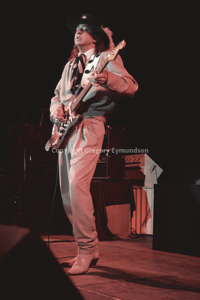 Musician performs passionately on stage, wearing a cowboy hat and unique outfit, showcasing vibrant guitar skills during a live concert.